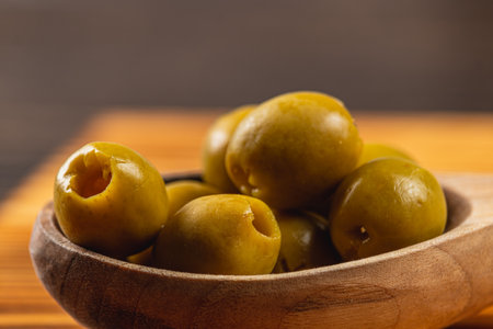 Freshly harvested green olives are beautifully displayed in a rustic wooden bowl, adding a touch of warmth and comfort to the cozy kitchen decor.の写真素材