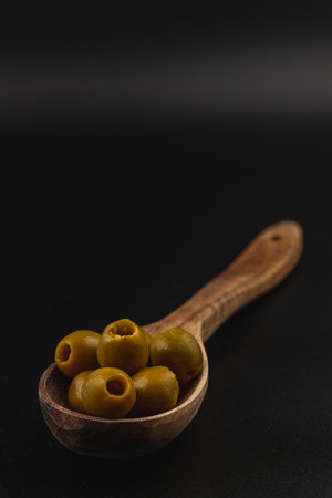 A wooden spoon holds several green olives, showcasing their smooth texture and unique shape. The dark background highlights the olives' natural color.の写真素材