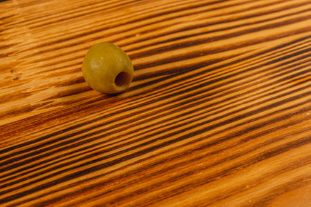 A single green olive rests on a beautifully grained wooden surface, evoking a comfortable kitchen atmosphere.の写真素材