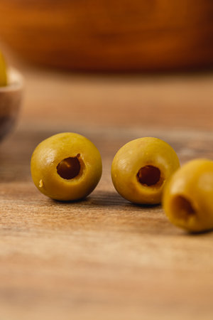 Three green olives with pitted centers rest on a wooden table, showcasing their smooth texture and natural color. A rustic bowl is visible in the background, adding warmth.の写真素材