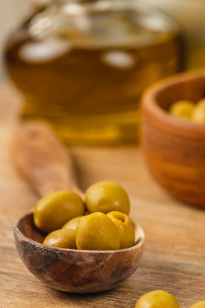 Green olives are arranged in a small wooden bowl, with a drizzle of olive oil visible in the background, creating an inviting culinary atmosphere in a rustic kitchen.の写真素材