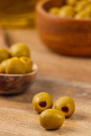 A collection of green olives is displayed on a rustic wooden surface. Some olives are placed in a small bowl, creating an inviting and fresh atmosphere. Natural lighting enhances the colors.の写真素材