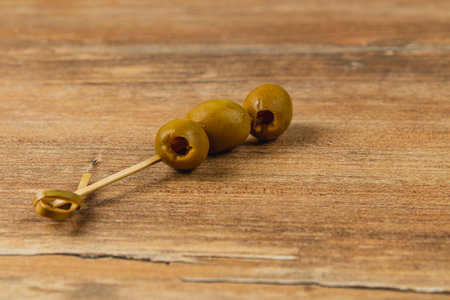 Three olives on a toothpick rest on a rustic wooden surface, perfect for a casual dining experience. Ideal for snacks at gatherings, they offer a savory taste.の写真素材