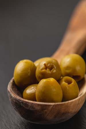 A collection of green olives fills a carved wooden bowl, showcasing their glossy texture. The dark background emphasizes the rich green color and organic shape.の写真素材