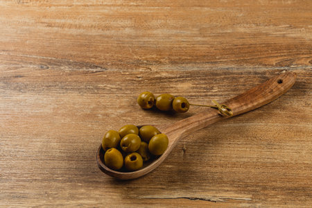 Fresh green olives rest in a wooden spoon on a weathered wooden surface, showcasing their rich color and smooth texture while highlighting a natural look and feel of the setting.の写真素材