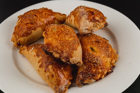 A plate holds an assortment of baked pumpkin pastries. Their golden-brown crusts and sugary tops suggest a warm, sweet treat perfect for autumn gatherings or dessert.の写真素材