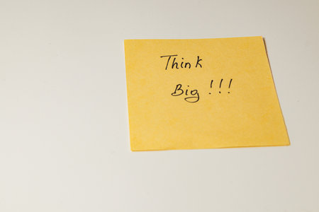 A yellow sticky note with the words Think Big !!! is placed on a clean workspace table. This serves as an encouraging reminder for creativity and ambition during work.の写真素材