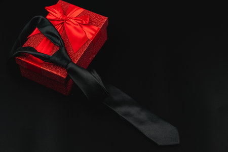 A black tie is elegantly draped over a festive red gift box adorned with a bow, symbolizing the joy of celebrating father's day or a birthday.の写真素材