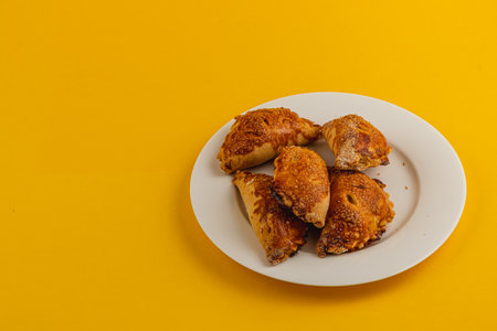 Golden pastries are arranged attractively on a round white plate, showcasing their flaky texture and delicious filling set against a vibrant yellow backdrop.の写真素材
