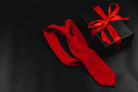 A red tie lies next to a beautifully wrapped black gift box adorned with a red ribbon. This arrangement symbolizes celebration and the joy of gifting on Father's Day or a birthday.の写真素材