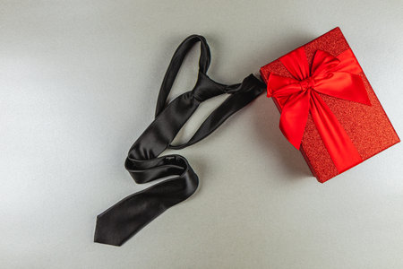 A stylish black tie is elegantly placed beside a vibrant red gift box adorned with a large bow. This scene captures the essence of Father's Day celebrations, perfect for honoring fathers.の写真素材