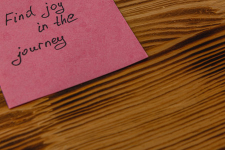 A bright pink sticky note rests on a wooden surface, featuring a handwritten message that encourages finding joy in the journey of life, promoting positivity and mindfulness.の写真素材