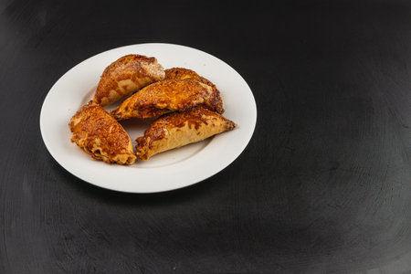 Golden pastries sit on a white plate against a black background. The pastries have a crispy surface, inviting anyone to take a bite and enjoy their sweetness.の写真素材