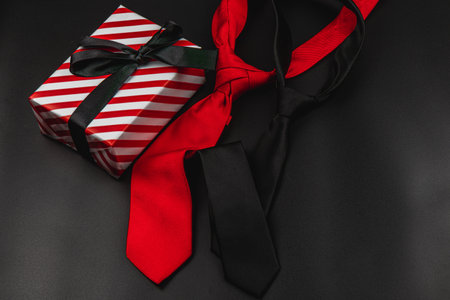 A beautifully wrapped gift box sits beside two stylish ties, one red and one black, symbolizing love and appreciation for fathers during birthday celebrations or father's day.の写真素材