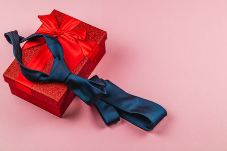 A festive celebration for Father's Day includes a vibrant red gift box topped with a large bow. A stylish blue tie rests beside the box, showcasing a thoughtful birthday gift for dads.の写真素材