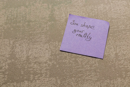 A purple note with a handwritten message sits on a neutral textured surface, conveying an empowering message about self-determination and perception of reality.の写真素材