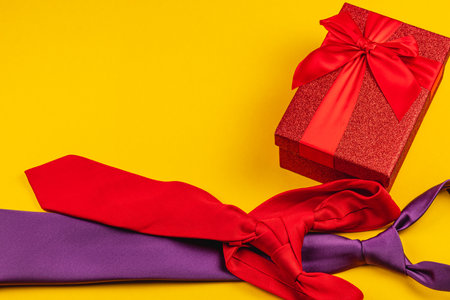 A vibrant arrangement showcases a red gift box adorned with a bow alongside colorful ties in shades of red and purple, perfect for celebrating Father's Day or a birthday.の写真素材