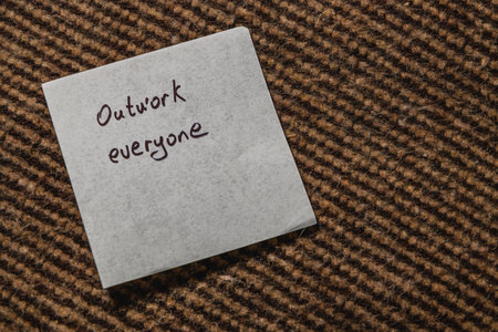 A handwritten note on a textured surface prompts everyone to outwork together, fostering a sense of unity and collaboration in a professional setting.の写真素材