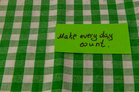 A bright green sticky note with the message to make every day count rests on a checkered cloth. This simple reminder promotes positivity in daily life and encourages mindfulness.の写真素材