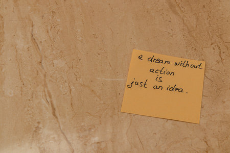 A close-up of a sticky note with an inspiring quote about dreams and action placed on a smooth, light-colored surface. The warm tones create a calm atmosphere.の写真素材