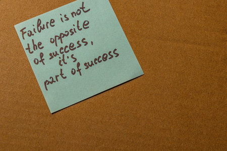A light blue sticky note is placed on a brown surface, featuring a motivational quote about failure and success.の写真素材