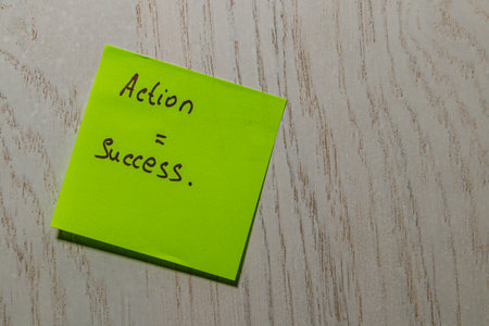 A bright yellow sticky note rests on a wooden surface, featuring the handwritten phrase that emphasizes the connection between action and success, inspiring an effective mindset.の写真素材