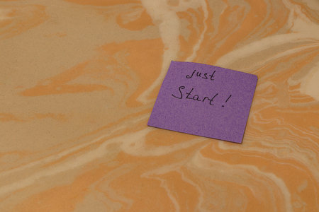 A purple note with the words just Start! is placed on a swirled, orange and beige surface, creating an inviting atmosphere for creativity and motivation.の写真素材