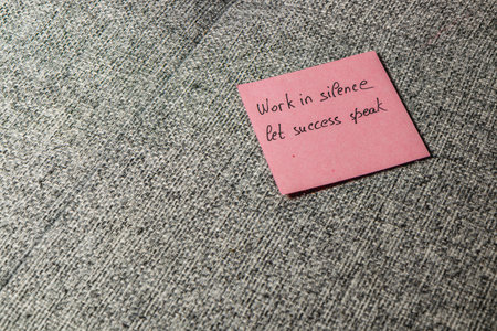 A pink sticky note with the motivational phrase Work in silence let success speak placed on a textured grey surface. This display emphasizes inspiration and focus on personal goals.の写真素材