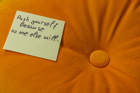 A bright orange cushion features a motivational note reminding individuals to push themselves for personal growth. The simple message promotes self-empowerment and initiative.の写真素材