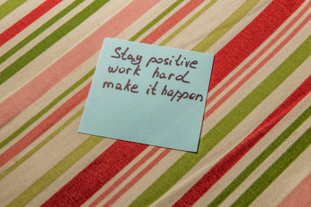 A handwritten note displaying the phrases Stay positive, Work hard, and Make it happen rests on a striped fabric. The message inspires productivity and a positive mindset.の写真素材