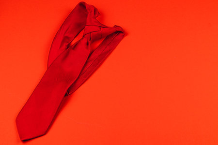 A vibrant red tie laid flat on an orange surface symbolizes thoughtful gifting for Father's Day or birthdays. This classic accessory highlights the celebration of fatherhood in style.の写真素材
