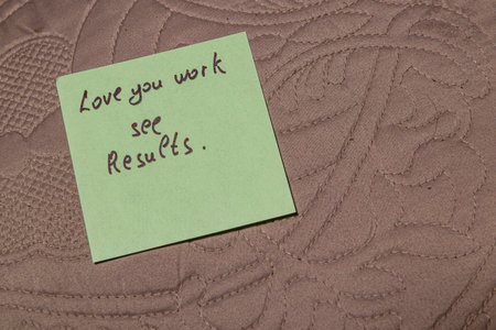 A green sticky note with handwritten words of encouragement is placed on a soft, textured surface, conveying a message about love, work, and results in a warm atmosphere.の写真素材