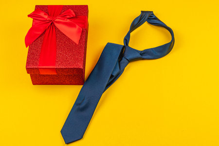 A vibrant celebration of father's day includes a neatly wrapped red gift box adorned with a ribbon next to a classic blue tie. This arrangement exemplifies thoughtful gifting for a special occasion.の写真素材