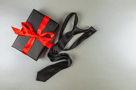This composition features a neatly wrapped black gift box with a red ribbon next to a black tie. Perfect for celebrating Father's Day or a birthday, conveying love and appreciation for fathers.の写真素材