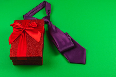 A vibrant red gift box tied with a bow sits next to a purple tie, perfect for Father's Day or a birthday celebration for fathers, showcasing love and appreciation for men.の写真素材