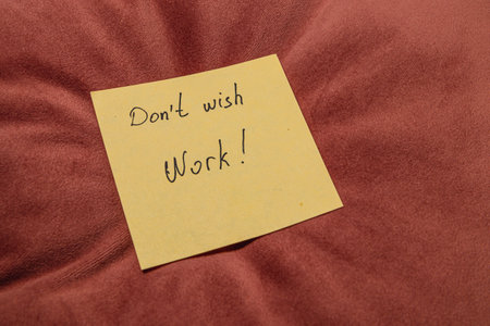 A bright yellow sticky note with handwritten text placed on a soft, reddish-brown cushion. The note conveys a motivational message.の写真素材