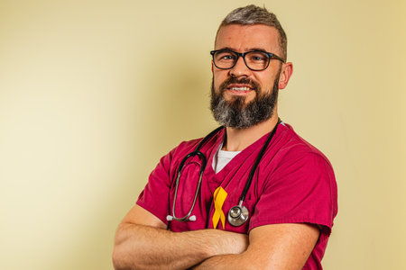 A young male cardiologist stands with arms crossed, smiling warmly. He wears glasses and has a stethoscope around his neck, signaling his dedication to patient care in a clinic.の写真素材