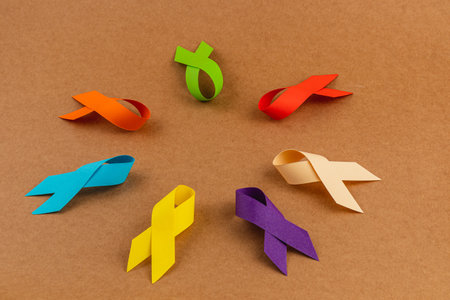 Brightly colored awareness ribbons are arranged on a brown surface, representing support for different cancers and diseases. These symbols promote health awareness and prevention globally.の写真素材