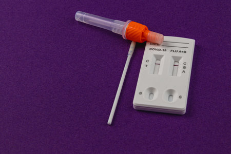 A COVID-19 and flu test kit sits on a purple surface, featuring a collection tube with an applicator and an easy-to-read results panel for effective health monitoring.の写真素材
