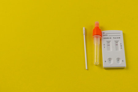A COVID-19 and flu testing kit is displayed on a vibrant yellow surface, with a swab and collection tube positioned alongside the test device for clear visibility.の写真素材