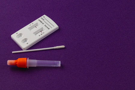 Display of a COVID-19 testing kit includes a test device, a swab for sample collection, and a sample container, set against a vibrant purple background for clarity.の写真素材