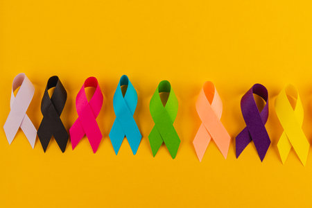 A vibrant display of awareness ribbons in multiple colors against a bright yellow background represents the ongoing battle against various diseases, promoting health and support for those affected.の写真素材