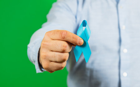 A person holds a blue awareness ribbon against a bright green background, symbolizing support for male health issues like prostate cancer, promoting awareness and prevention.の写真素材