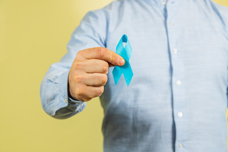 A man holds a blue ribbon symbolizing prostate cancer awareness. This campaign highlights the importance of health awareness and support for those affected by the disease.の写真素材