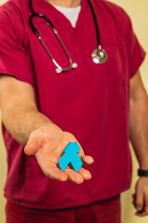 A male healthcare worker in pink scrubs holds a blue arrow symbol in his palm, representing support in patient care. He appears happy and engaged in his role within the clinic environment.の写真素材