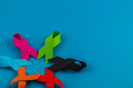 Multiple vibrant ribbons in pink, green, and other colors are arranged on a bright blue background, showcasing support for different health awareness campaigns, including cancer and diabetes.の写真素材