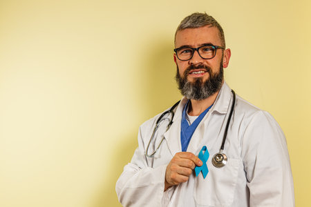 A male healthcare worker in scrubs and a lab coat proudly presents a teal awareness ribbon, smiling in a bright clinic space dedicated to supporting patients and promoting health.の写真素材