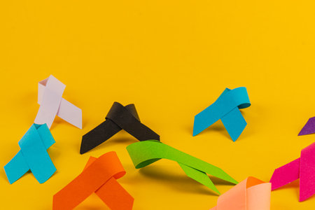 Various brightly colored awareness ribbons are scattered against a vibrant yellow background, representing multiple health campaigns and initiatives aimed at raising awareness and support.の写真素材
