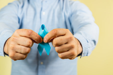 A person holds a blue awareness ribbon, symbolizing support for cancer initiatives. This moment highlights the importance of healthcare and advocacy in the fight against disease.の写真素材