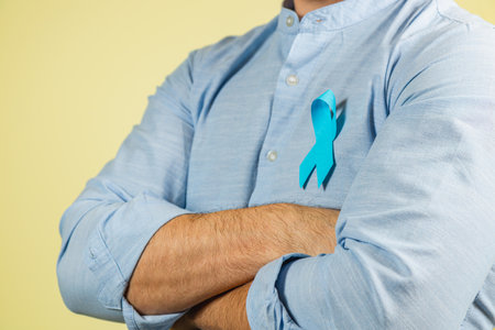 A man stands confidently with crossed arms, displaying a blue ribbon pinned to his shirt. This symbolizes support for prostate cancer awareness and health education.の写真素材